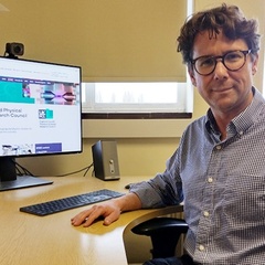 Image of dark haired man with glasses sitting at a desk with a computer monitor