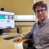 Image of dark haired man with glasses sitting at a desk with a computer monitor