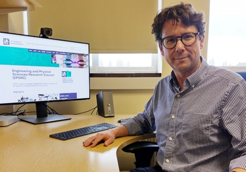 Image of dark haired man with glasses sitting at a desk with a computer monitor