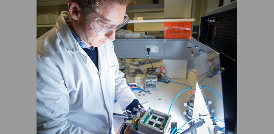 Image of man in labcoat wearing safety glasses working at a lab bench